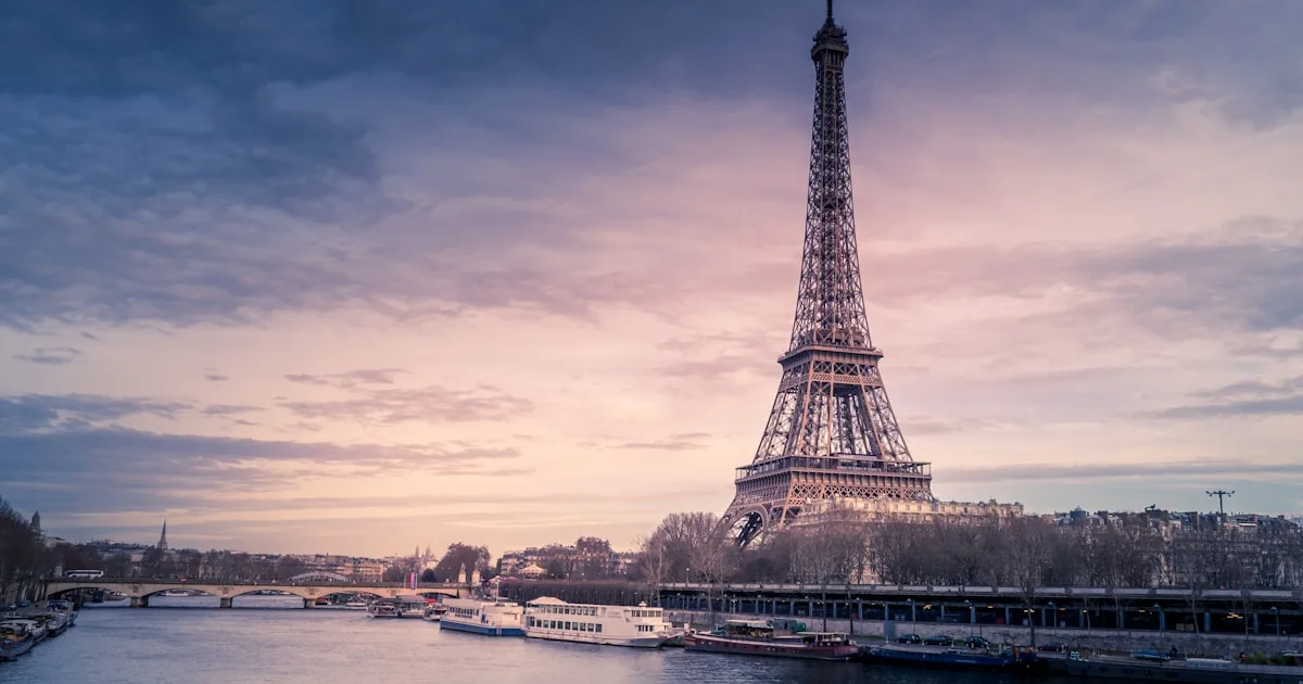 Chauffeur VTC professionnel en costume à côté d'une berline noire haut de gamme à Paris avec la Tour Eiffel en arrière-plan